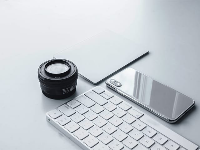 Camera lens, keyboard, smartphone, notepad on white desk